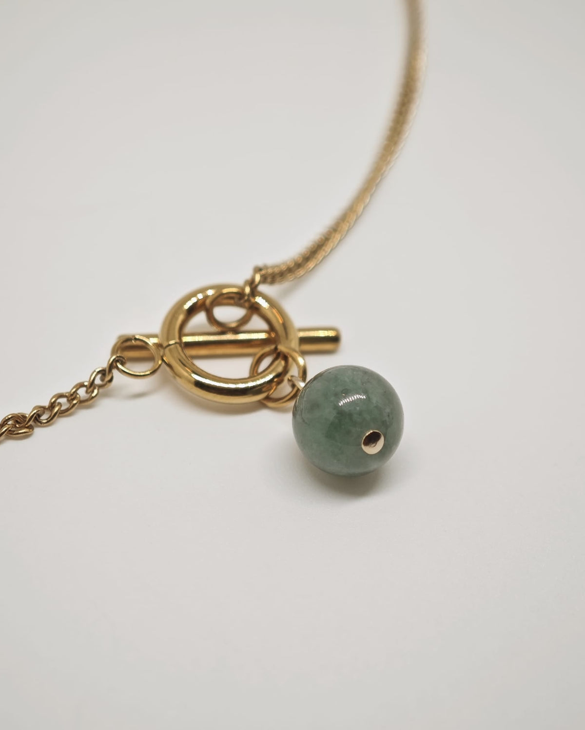 Gold necklace with a green bead on a white background