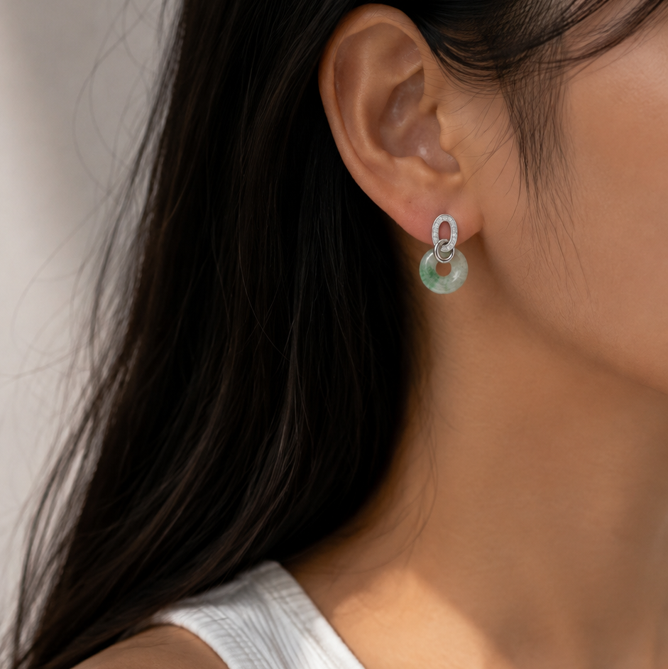 A close-up side profile of a woman with long black hair wearing a delicate silver hoop earring with a small light green circular charm.