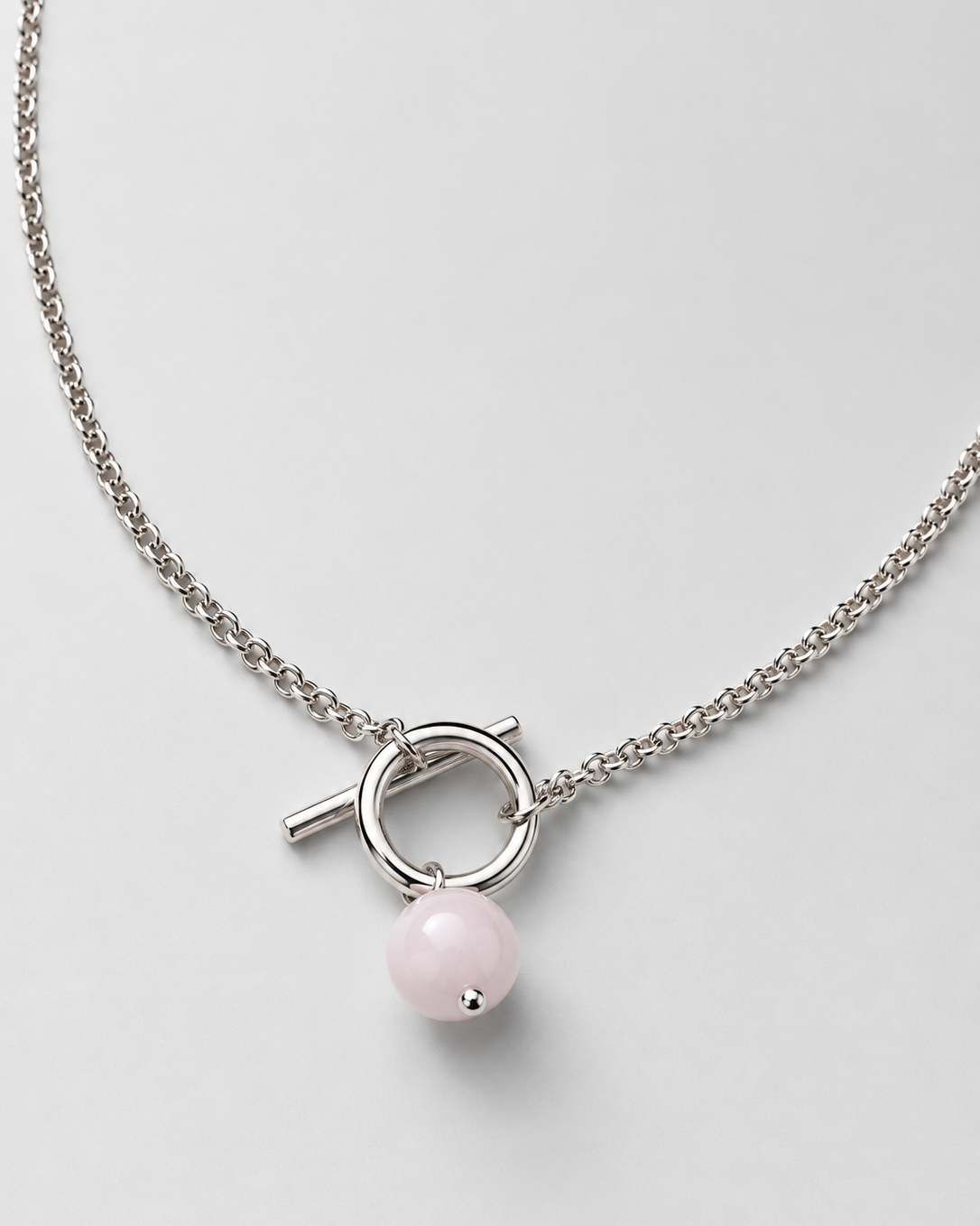 A silver-toned chain necklace featuring a toggle clasp with a small pink bead pendant, displayed on a light gray background.