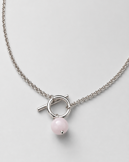 A silver-toned chain necklace featuring a toggle clasp with a small pink bead pendant, displayed on a light gray background.